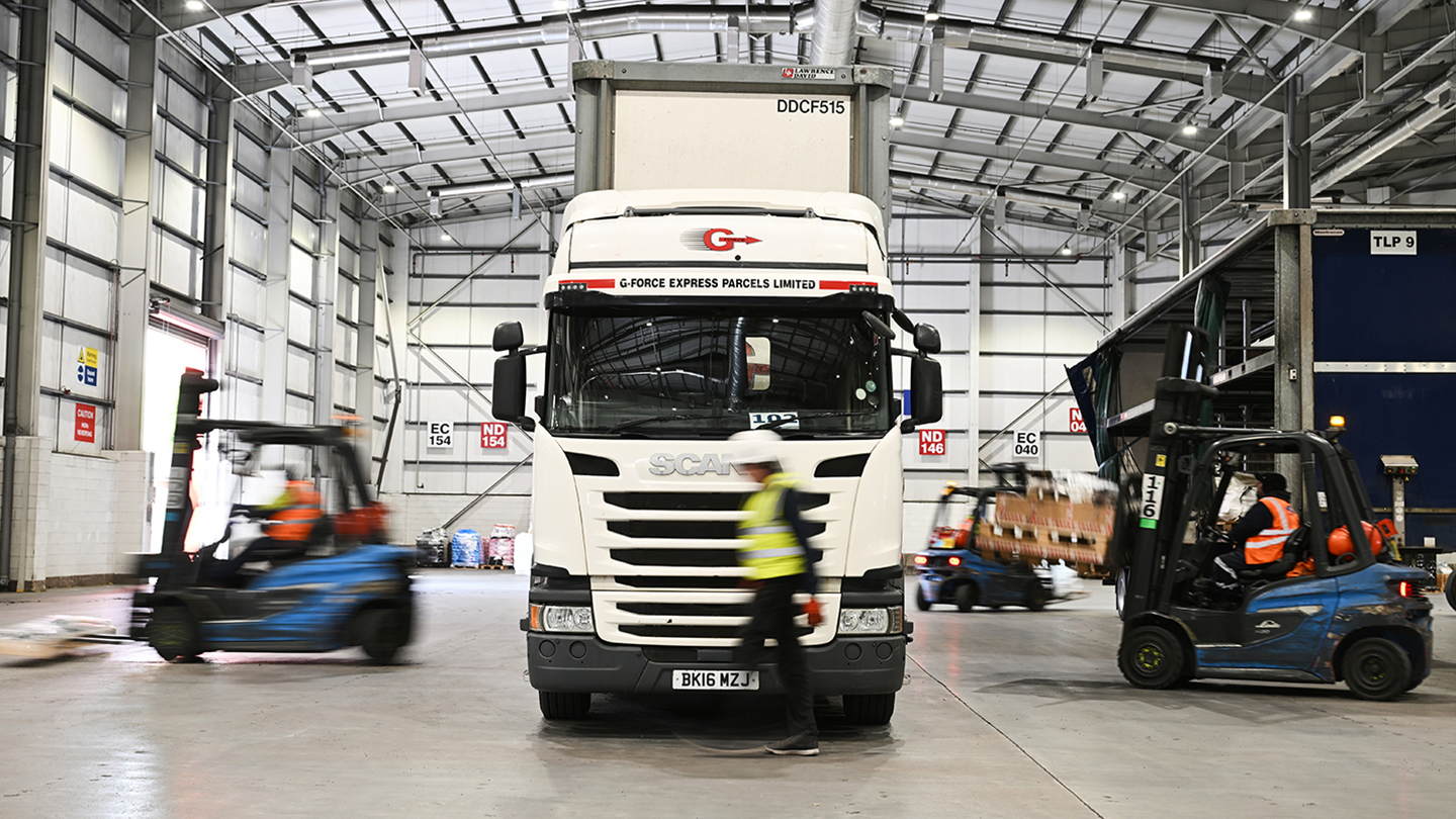 Image of a lorry and forklift vehicles, with a man walking past